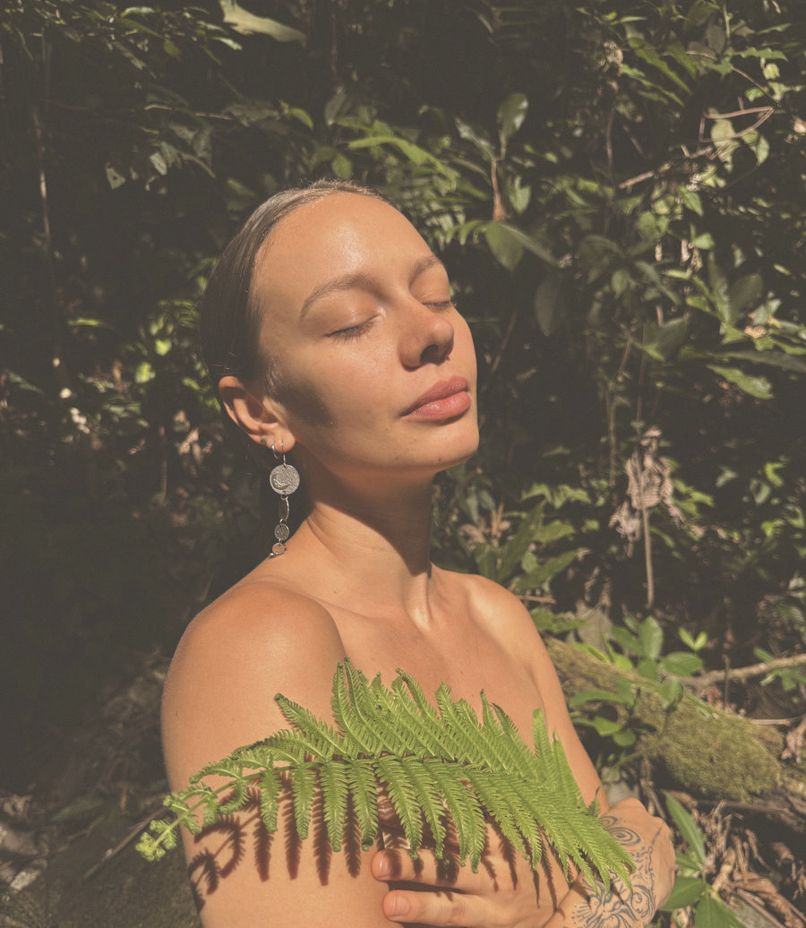 Skye with her eyes closed and her face lifted to the light, a fern frond held across her chest.